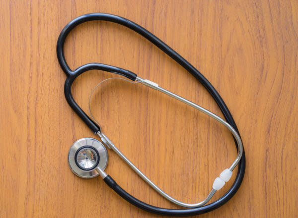 A black stethoscope rests on a wooden surface, viewed from above.