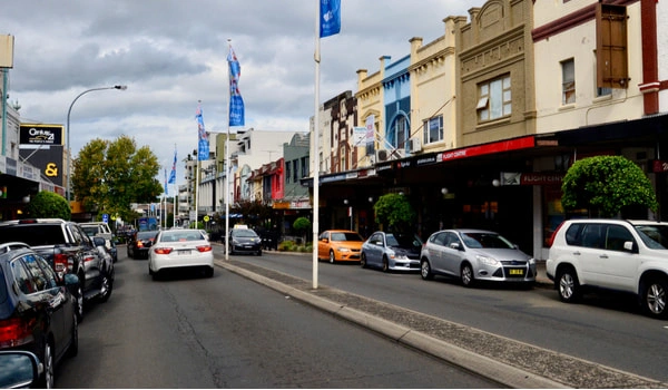 Marrickville Street scene with colourful storefronts, parked cars on both sides, and banners along the sidewalk in Marrickville town center.