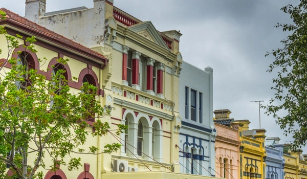Colourful row of historic townhouses in Surry Hills, Sydney with ornate façades along a tree-lined street on a cloudy day.